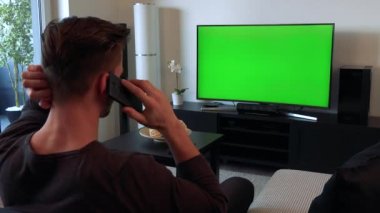 Bir adam bir smartphone üzerinde görüşmeler ve yeşil bir ekran bir Tv izliyor