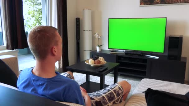 Un uomo guarda una TV con uno schermo verde in un accogliente soggiorno — Video Stock