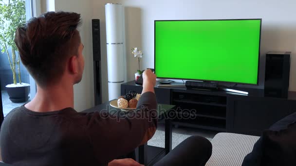 Человек щелкает контроллером по телевизору с зеленым экраном и качает головой несчастливо — стоковое видео