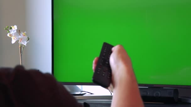 Рука щелкает контроллером по телевизору с зеленым экраном — стоковое видео