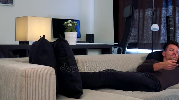 Genç ve yakışıklı bir adam rahat oturma odası saatler kamera kapalı olan bir Tv bir kanepede yatıyor — Stok video