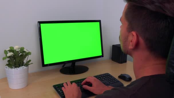 Un hombre escribe en una computadora con una pantalla verde — Vídeos de Stock