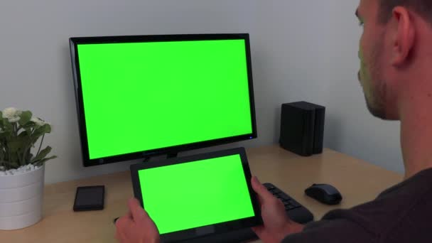 En man klockor i vänder sin surfplatta och en datorskärm, båda gröna skärmar — Stockvideo