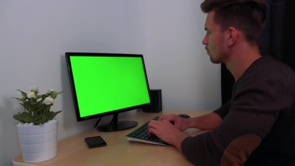 Un hombre joven y guapo escribe en una computadora con una pantalla verde — Vídeos de Stock