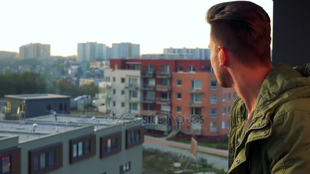 Een jonge, knappe man staat op een balkon en uitkijkt — Stockvideo