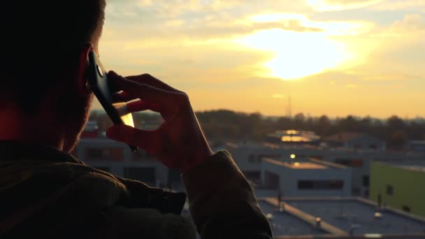 Un hombre habla en el teléfono inteligente y observa la puesta de sol — Vídeos de Stock