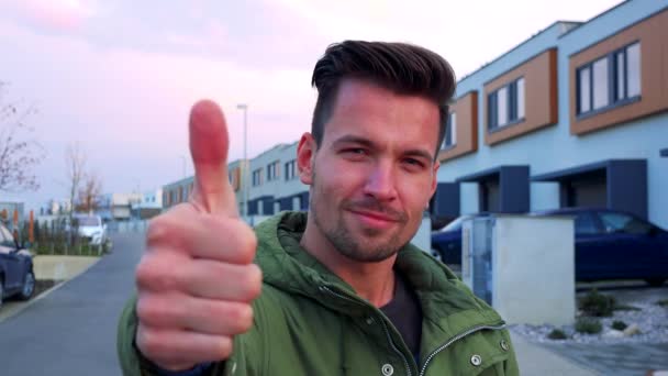 A young, handsome man stands on a road and shows a thumb up to the camera, a street in the background — Stock Video