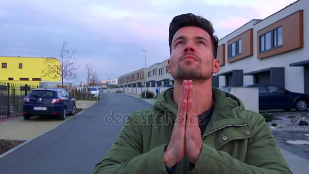 Ein junger, gutaussehender Mann steht auf einer Straße, betet und überquert sich selbst, eine Straße im Hintergrund — Stockvideo