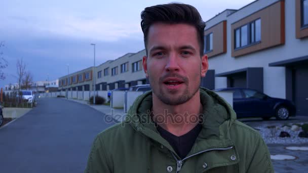 Ein junger, gutaussehender Mann spricht in die Kamera über eine Straße und Gebäude hinter ihm — Stockvideo