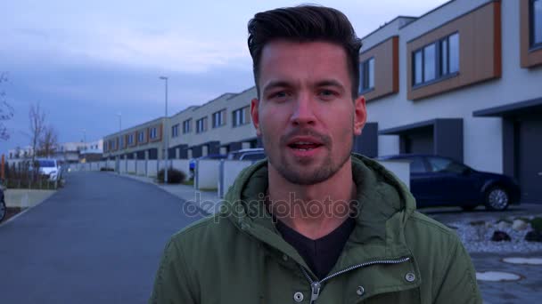 Un jeune homme beau parle à la caméra d'une rue et de bâtiments derrière lui. — Video