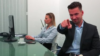 Genç ve yakışıklı bir adam gülümsüyor ve Puan bir ofiste meslektaşım eserleri arka planda bir bilgisayarda kameraya