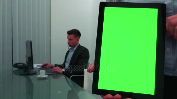 Ein Tablet mit grünem Bildschirm - Nahaufnahme, ein Geschäftsmann arbeitet am Computer im Hintergrund — Stockvideo