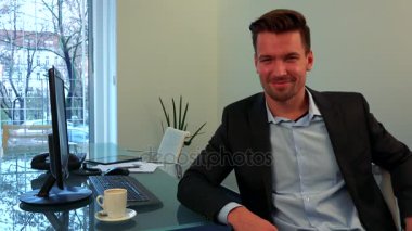 Genç ve yakışıklı bir adam bir ofis, herkes hata yapabilir ve kamera gülümser bir masada oturur