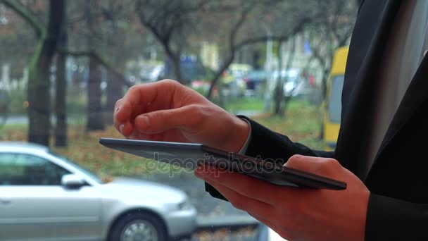 Um homem trabalha em um tablet - close-up nas mãos, uma rua no fundo — Vídeo de Stock