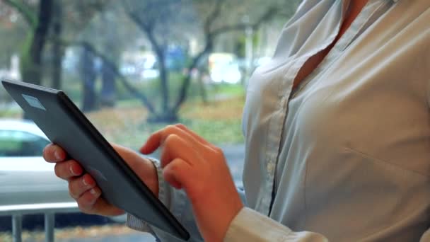 Una mujer trabaja en una tableta - primer plano en las manos, una calle en el fondo — Vídeo de stock