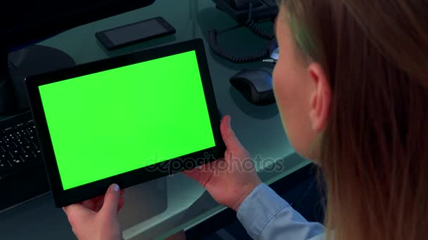 Een vrouw kijkt naar een tablet met een groen scherm in een kantoor — Stockvideo