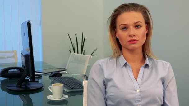 Eine junge, schöne Frau sitzt an einem Schreibtisch in einem Büro und blickt in die Kamera — Stockvideo