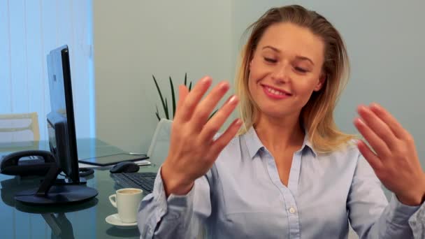 Mladá, krásná žena sedí za stolem v kanceláři, usměje se na kameru a ukazuje gesto Pozvánka — Stock video