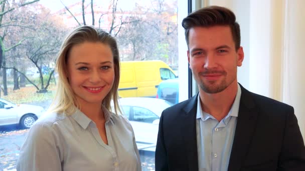男と女 (若い、魅力的な) オフィスとカメラで笑顔のウィンドウによって立つ — ストック動画