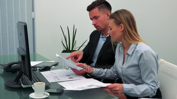 Egy férfi és egy nő (fiatal és vonzó) ülni egy asztal, egy iroda, beszélni, és csinál a papírmunka — Stock videók