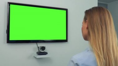 Yeşil televizyon ekranında bir kadın (başının arkasına kameraya) görünüyor