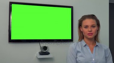 Kamera, arka planda yeşil televizyon ekranı, genç, güzel bir kadın bakar