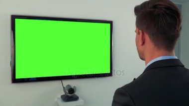 Takım elbiseli bir adam bir yeşil televizyon ekranında görünüyor