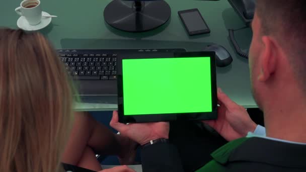 Een man en een vrouw op een bureau in een kantoor zitten en kijken naar een tablet met een groen scherm — Stockvideo