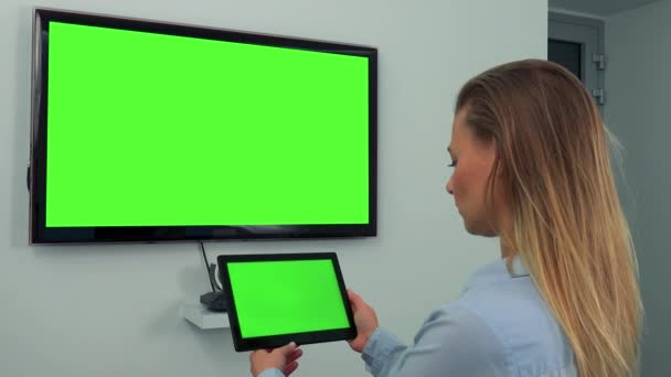 Een vrouw kijkt in bochten bij een groene TV-scherm en een tablet met een groen scherm — Stockvideo