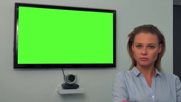 A young, beautiful woman shakes her head at the camera, a green television screen in the background — Stock Video