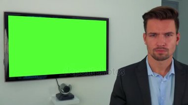 Kamera, arka planda yeşil televizyon ekranı elbiseli bir genç, yakışıklı adam bakar