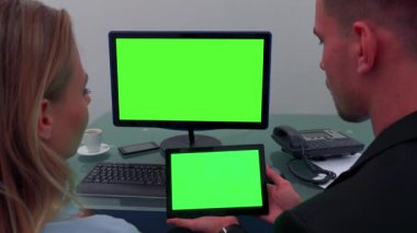 Bir erkek ve bir kadın bir ofiste bir masada oturup ve döner bir bilgisayar ekranı ve bir tablet (her iki yeşil ekran bak)