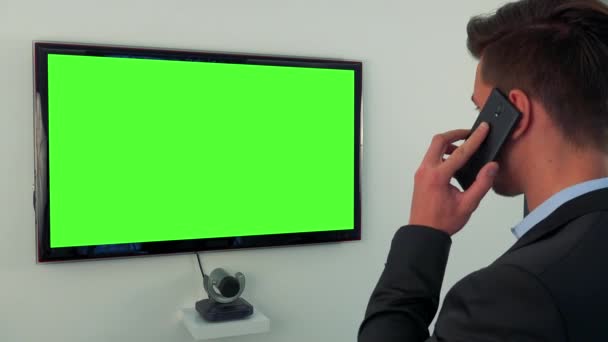 Un uomo parla su uno smartphone davanti a uno schermo verde della televisione — Video Stock