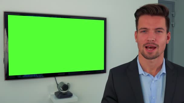 Un hombre joven y guapo en traje habla con la cámara, una pantalla de televisión verde en el fondo — Vídeos de Stock