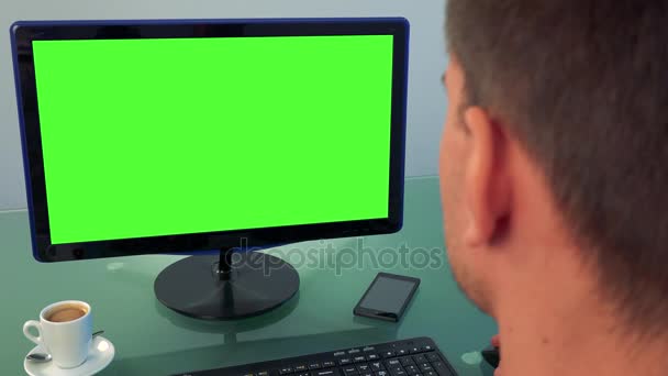 Een man (de achterkant van zijn hoofd naar de camera) werkt op een computer met een groen scherm — Stockvideo