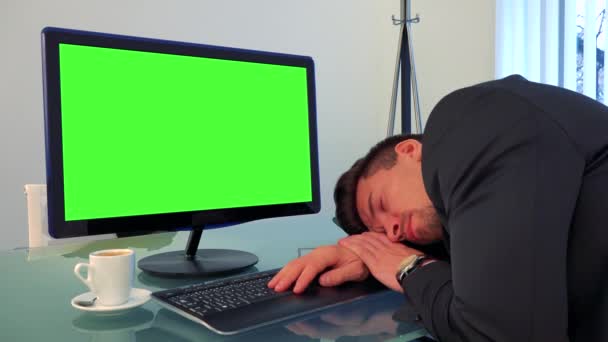 En ung, stilig man sover på ett skrivbord framför en grön dataskärm — Stockvideo