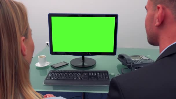 Um homem e uma mulher sentam-se em frente a um computador com uma tela verde em um escritório, observam a tela e falam — Vídeo de Stock
