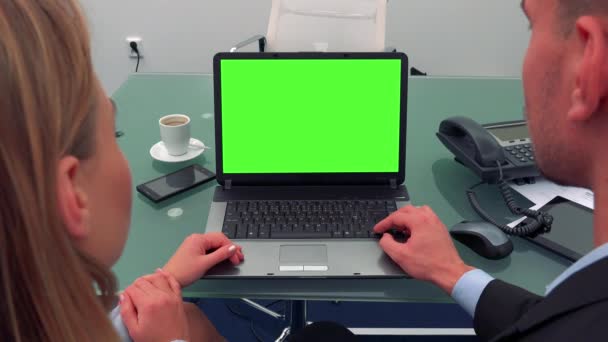 Un uomo e una donna siedono davanti a una scrivania davanti a un notebook con uno schermo verde in un ufficio, guardano lo schermo e parlano — Video Stock