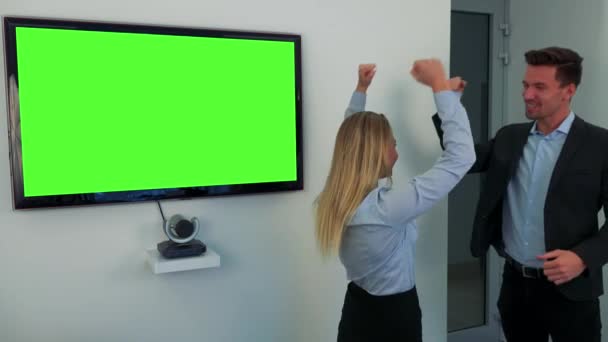 Un hombre y una mujer celebran frente a una pantalla de televisión verde — Vídeos de Stock