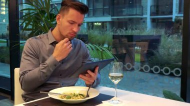 Genç ve yakışıklı bir adam bir tablete bir restoran ve çalışan bir masada oturur