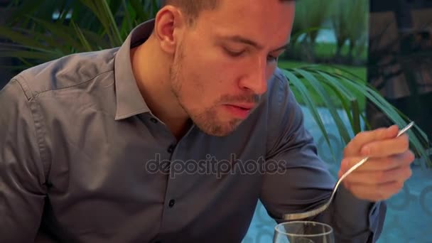 若く、ハンサムな男がレストランのテーブルに座っているし、パスタを食べる — ストック動画