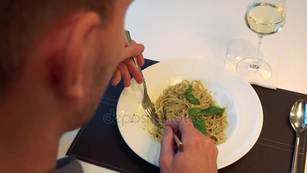 Een man zit aan een tafel in een restaurant en eet pasta — Stockvideo