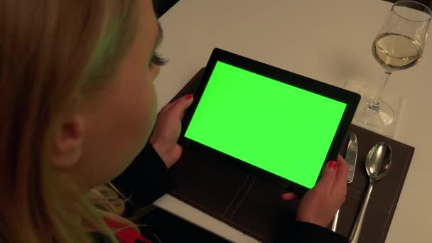 Женщина сидит за столом в ресторане и смотрит на планшет с зеленым экраном — стоковое видео