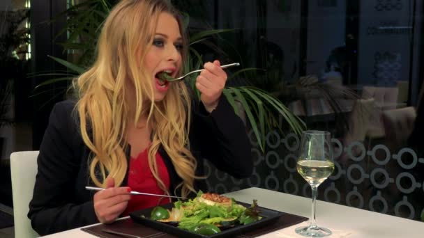 Μια νεαρή, όμορφη γυναίκα που κάθεται σε ένα τραπέζι σε ένα εστιατόριο και απολαμβάνει μια σαλάτα — Αρχείο Βίντεο