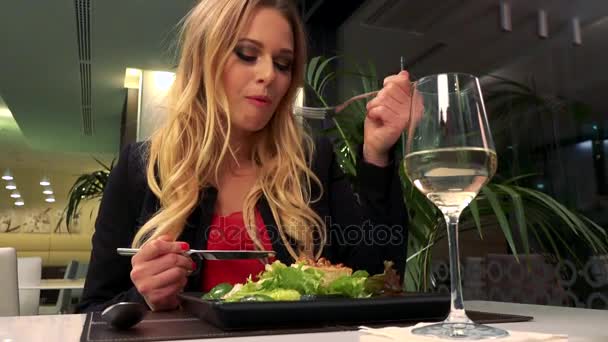 En ung, vacker kvinna sitter vid ett bord på en restaurang och äter en sallad — Stockvideo