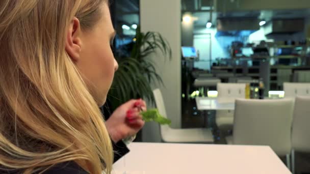 Een jonge, mooie vrouw zit aan een tafel in een restaurant en eet — Stockvideo