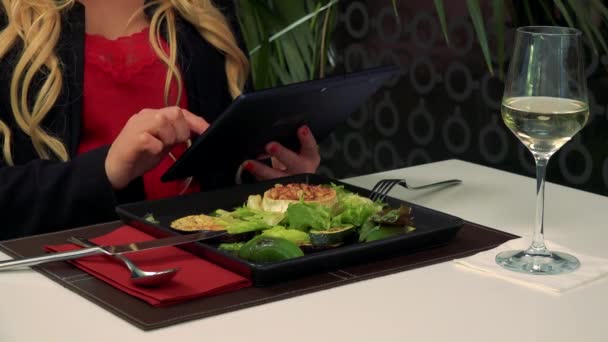 Bir kadın bir restoran ve çalışan bir masada bir tablet, salata ve bir bardak şarap onun önünde oturur — Stok video