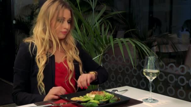 Una giovane donna attraente si siede a un tavolo in un ristorante e aspetta un cameriere, impaziente — Video Stock