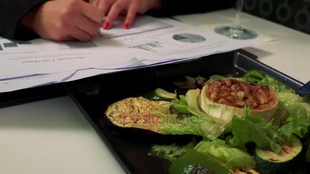 Uma mulher senta-se a uma mesa em um restaurante e escreve em um papel, uma salada na frente dela — Vídeo de Stock