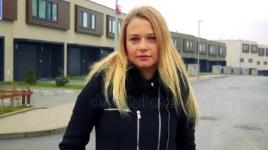 Genç, güzel bir kadın sokakta duruyor ve kameraya, binalar içinde belgili tanımlık geçmiş görünüyor